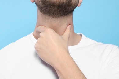 Man suffering from sore throat on light blue background, closeup