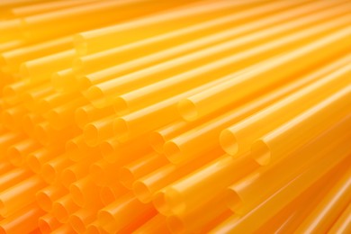 Photo of Heap of yellow plastic straws for drinks as background, closeup