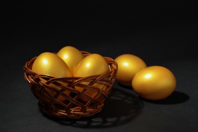 Photo of Shiny golden eggs and wicker bowl on black background