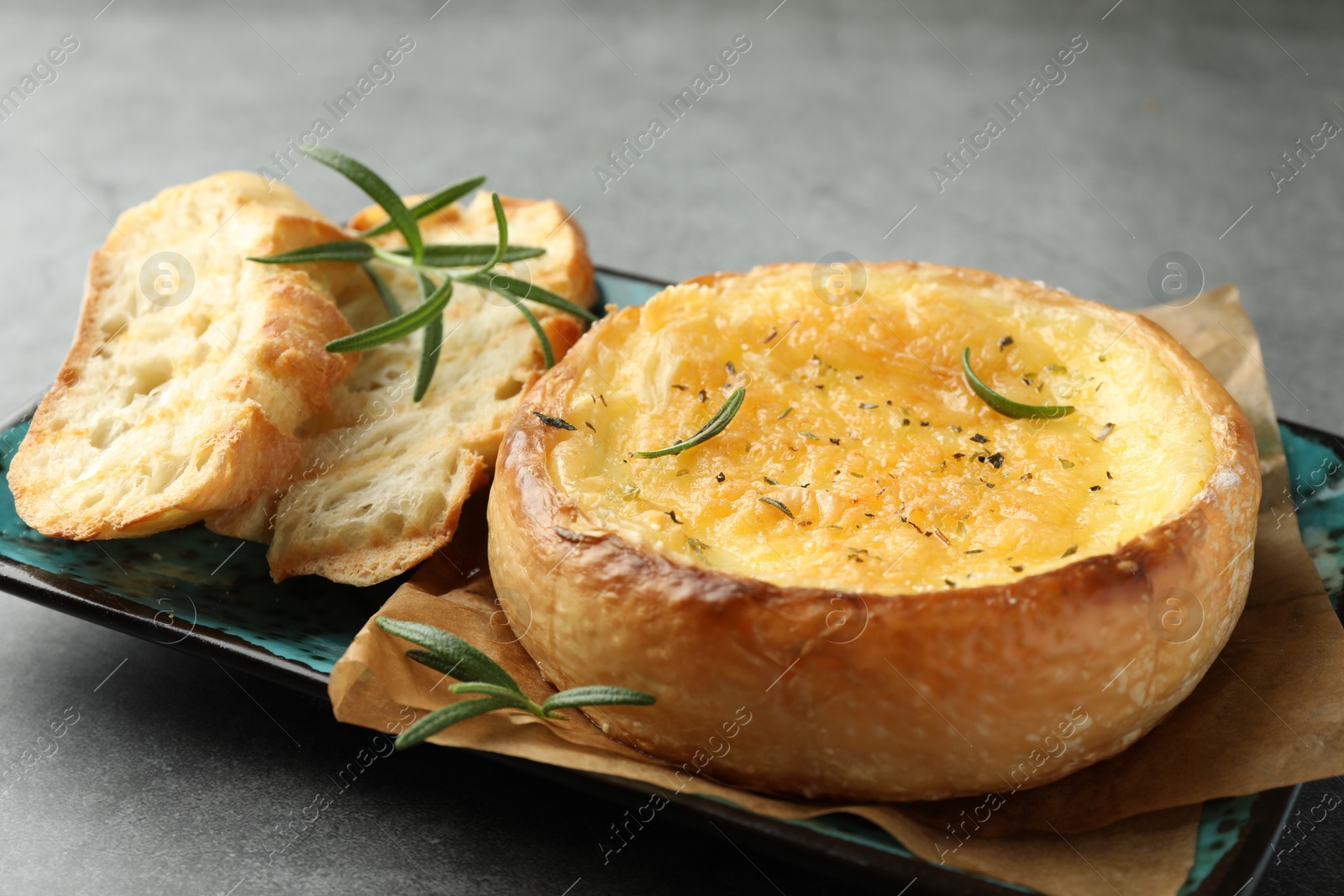 Photo of Plate with tasty baked brie cheese, bread and rosemary on grey table, closeup