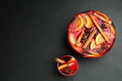 Photo of Glass and bowl of delicious aromatic punch drink on black table, flat lay. Space for text