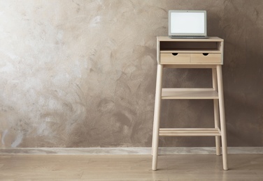 Photo of High wooden table with laptop as stand up workplace near color wall
