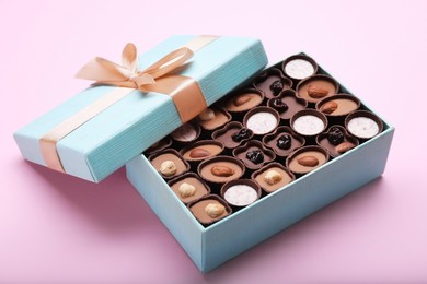 Photo of Open box of delicious chocolate candies on pink background, closeup