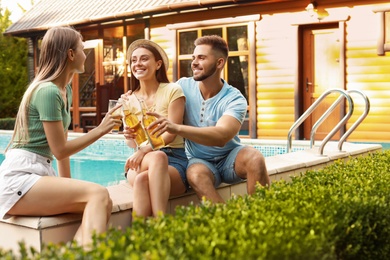 Happy friends with drinks at barbecue party near swimming pool outdoors