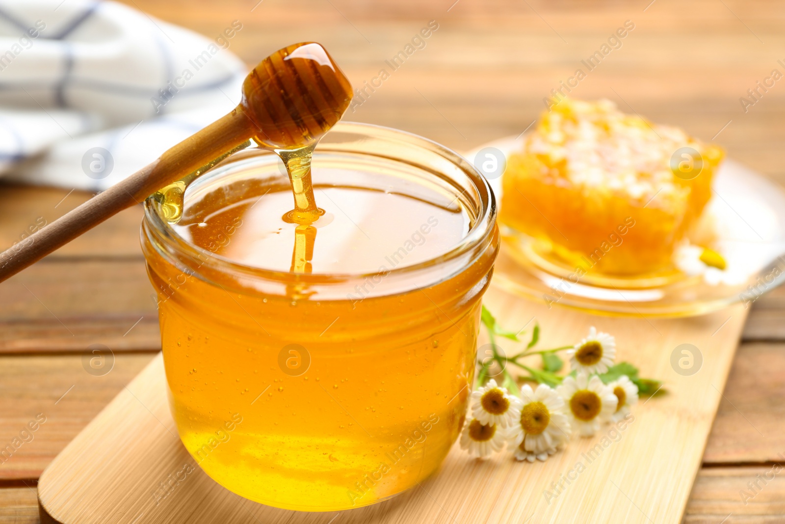 Photo of Honey dripping from dipper into jar on wooden table, closeup