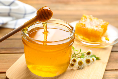 Photo of Honey dripping from dipper into jar on wooden table, closeup