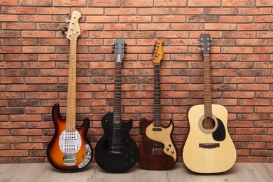 Photo of Modern electric and classical guitars near red brick wall indoors