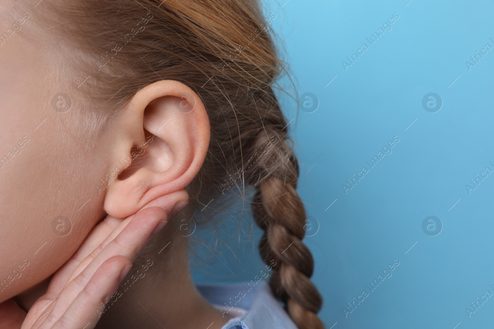 Photo of Cute little girl showing hand to ear gesture on light blue background, closeup. Space for text