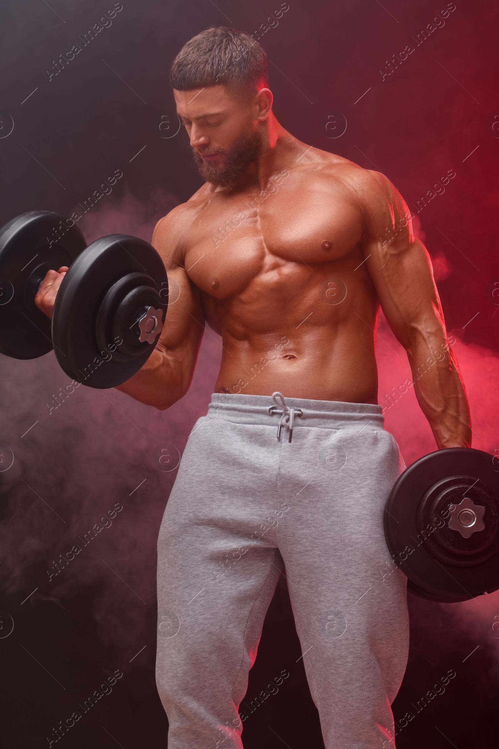 Photo of Young bodybuilder exercising with dumbbells in smoke on color background, low angle view