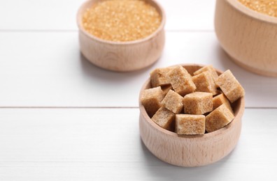 Photo of Different types of brown sugar in bowls on white wooden table, closeup. Space for text