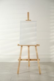 Photo of Wooden easel with blank canvas near light wall