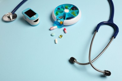 Photo of Stethoscope, pills and fingertip pulse oximeter on light blue background, space for text. Medical gift
