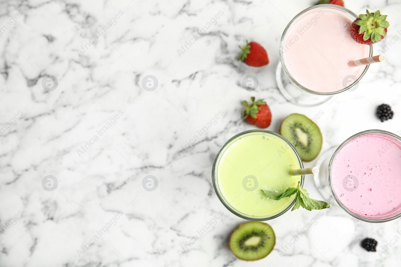 Photo of Tasty fresh milk shakes with fresh berries on white marble table, flat lay. Space for text