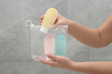 Woman packing cosmetic travel kit near grey wall closeup. Bath accessories