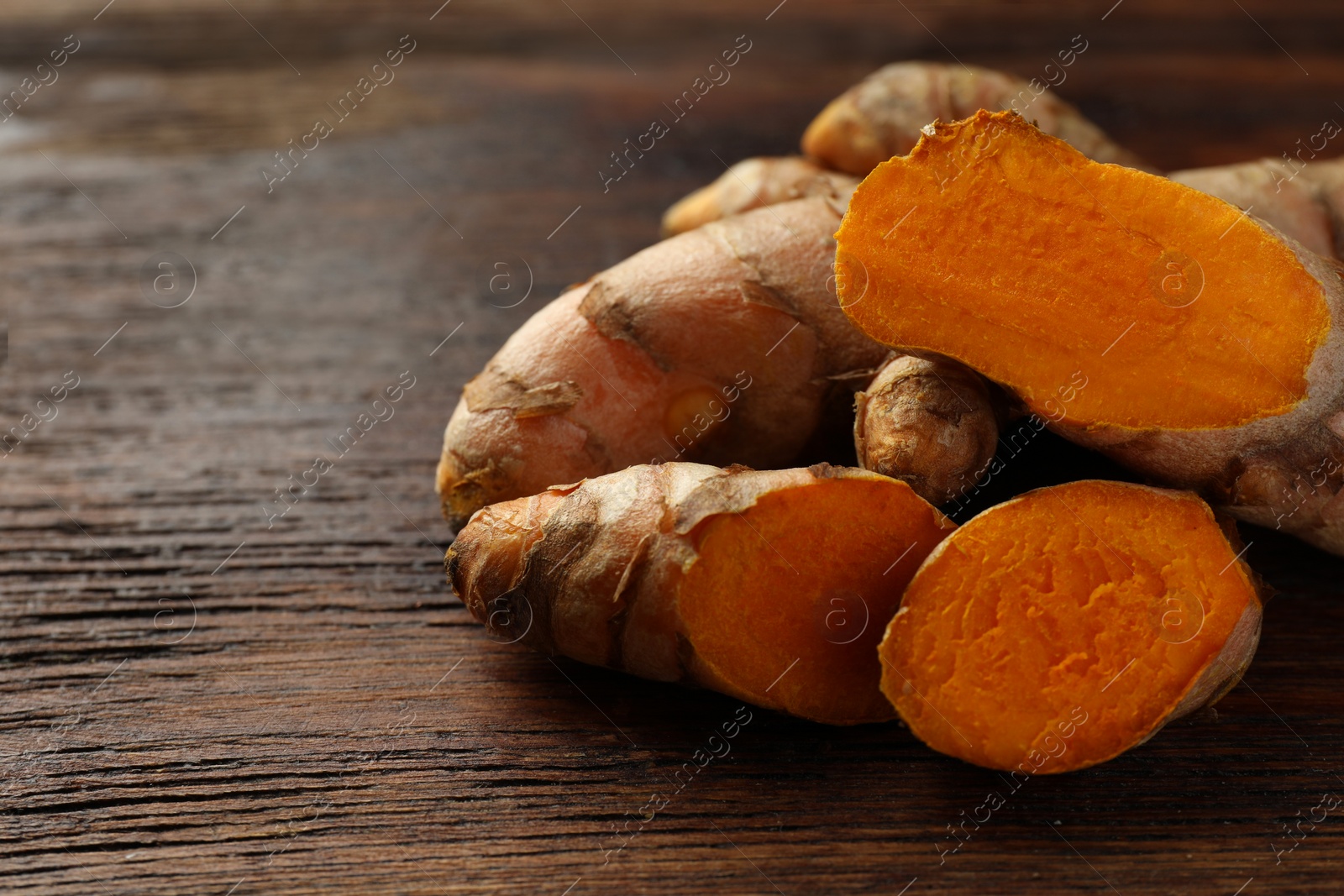 Photo of Fresh turmeric roots on wooden table, closeup. Space for text