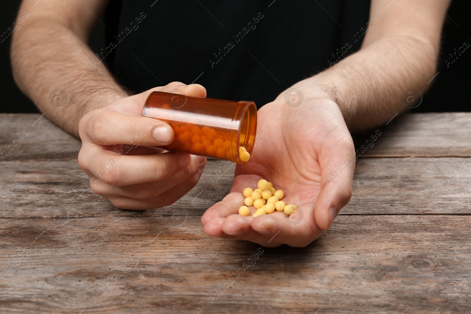 Photo of Man pouring pills out of bottle into hand at table, closeup