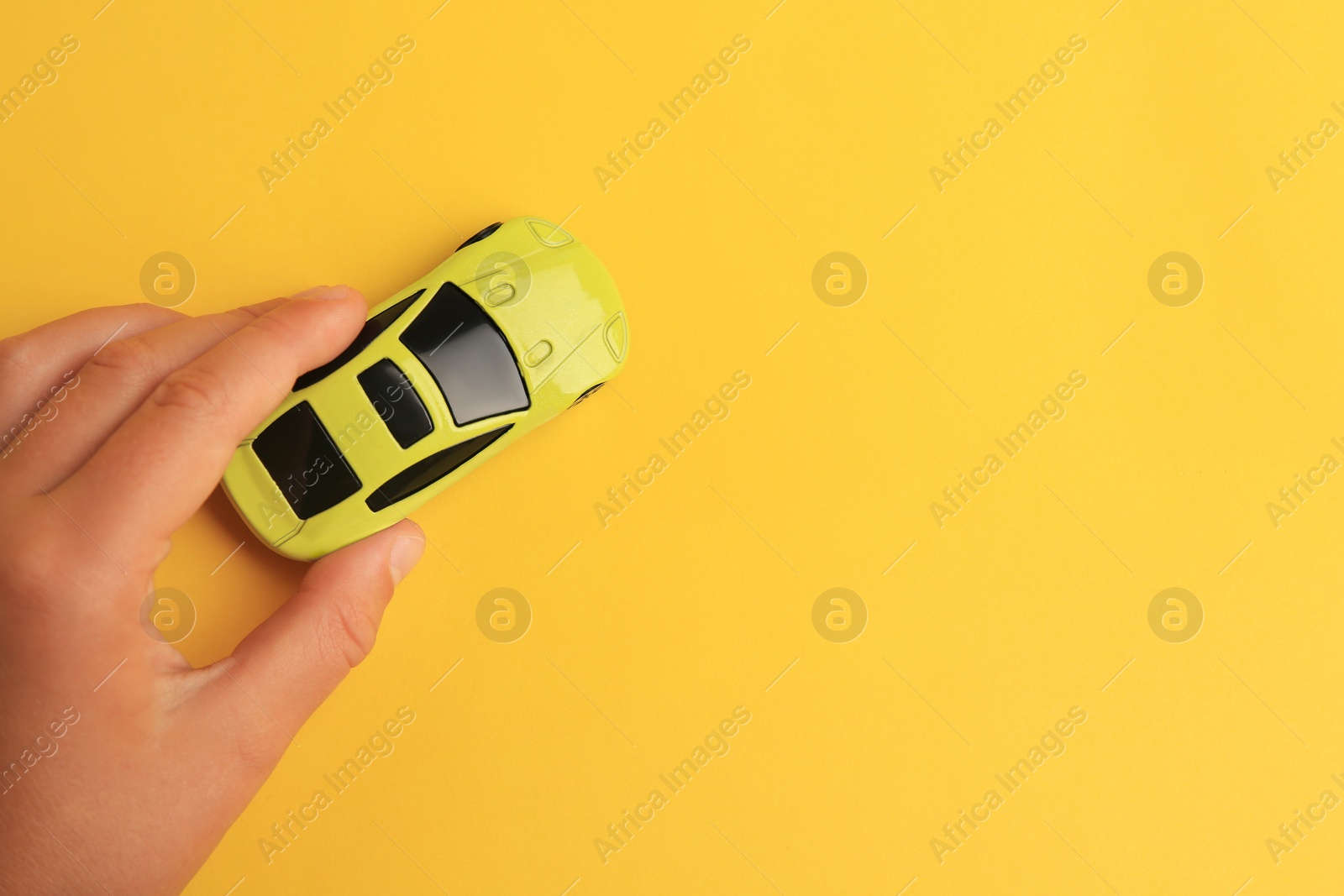 Photo of Child playing with toy car on yellow background, top view. Space for text