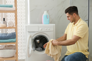 Photo of Man with clothes near washing machine in bathroom. Laundry day