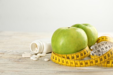 Photo of Jar of weight loss pills, apples and measuring tape on white wooden table