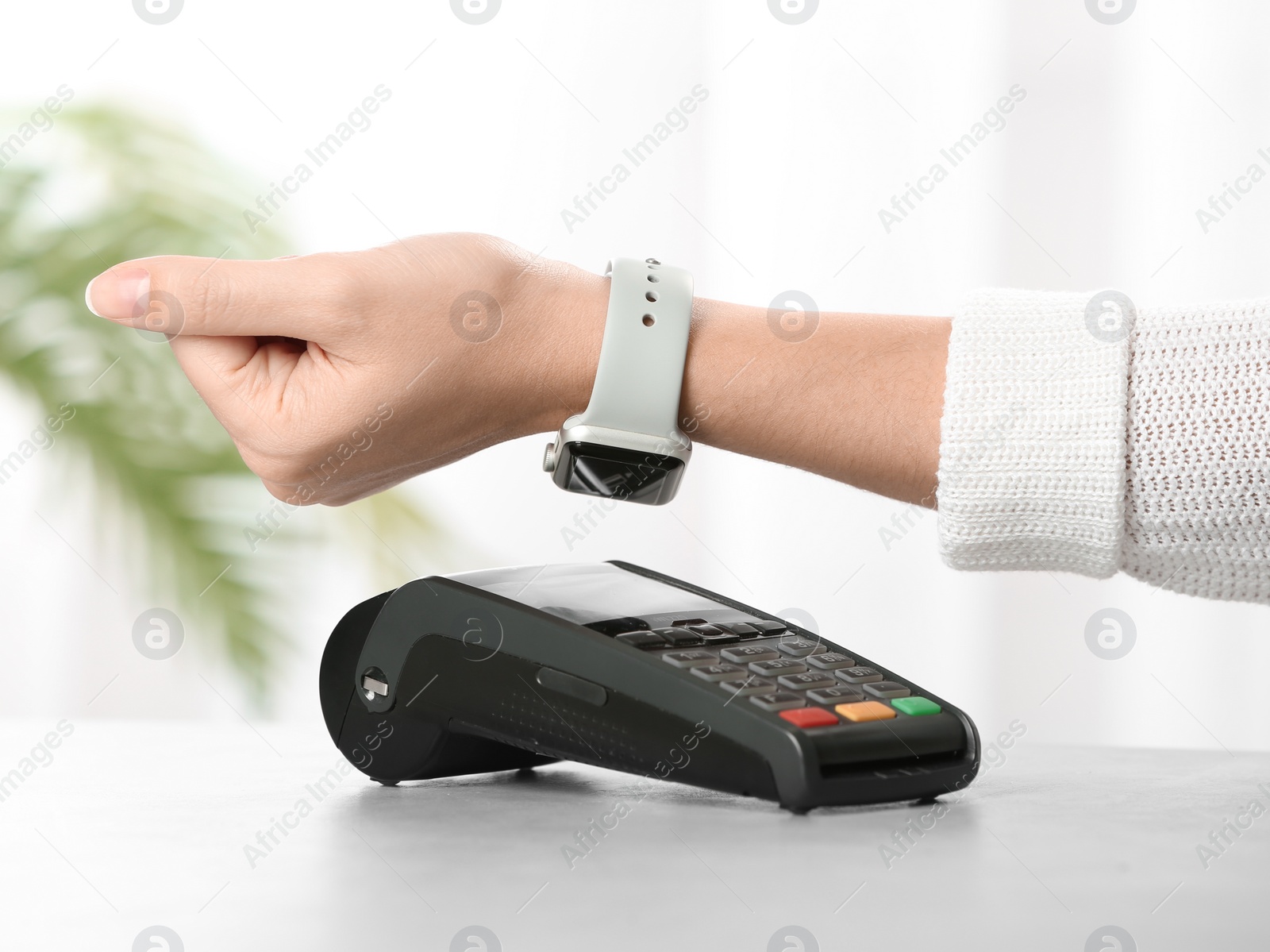 Photo of Woman using terminal for contactless payment with smart watch at table, closeup