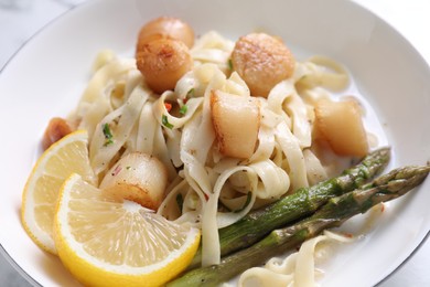 Photo of Delicious scallop pasta with asparagus and lemon on table, closeup