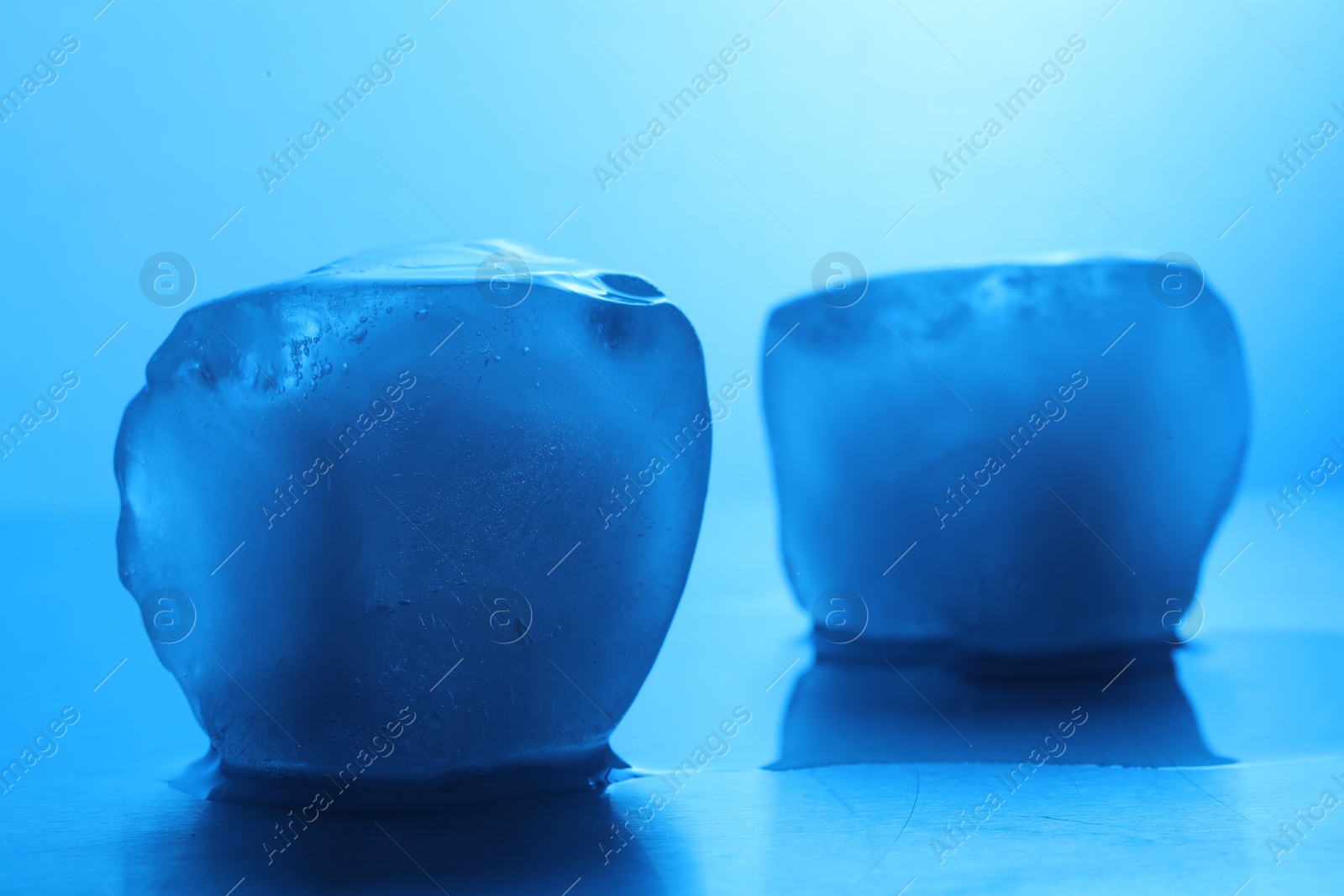 Photo of Crystal clear ice cubes on light blue background, closeup. Color tone effect