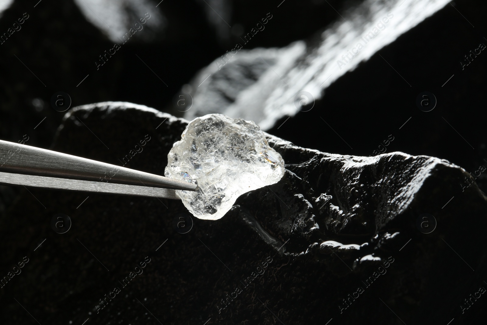 Photo of Tweezers with beautiful shiny diamond over stones, closeup