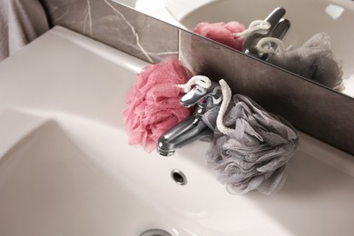 Photo of Colorful shower puffs between faucet on sink in bathroom, above view