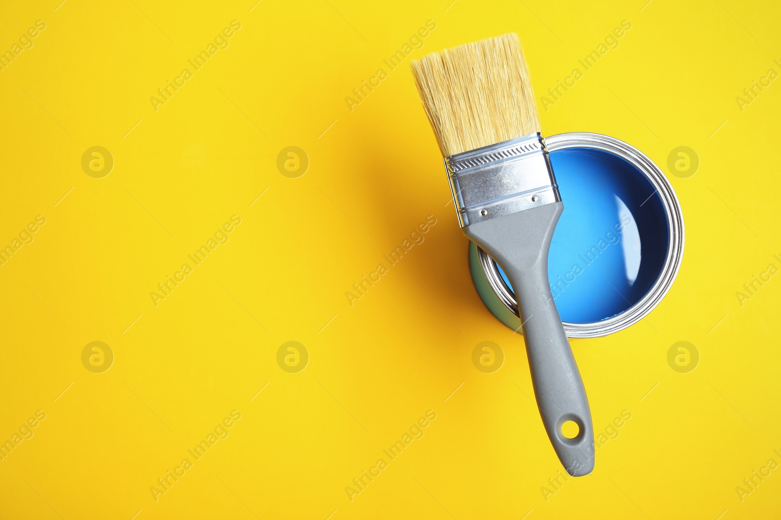 Photo of Paint can and brush on yellow background, top view. Space for text