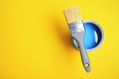 Photo of Paint can and brush on yellow background, top view. Space for text