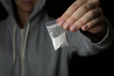 Photo of Drug dealer holding bag with cocaine on black background, closeup