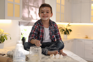 Photo of Cute little boy with flour on face in kitchen. Cooking dough