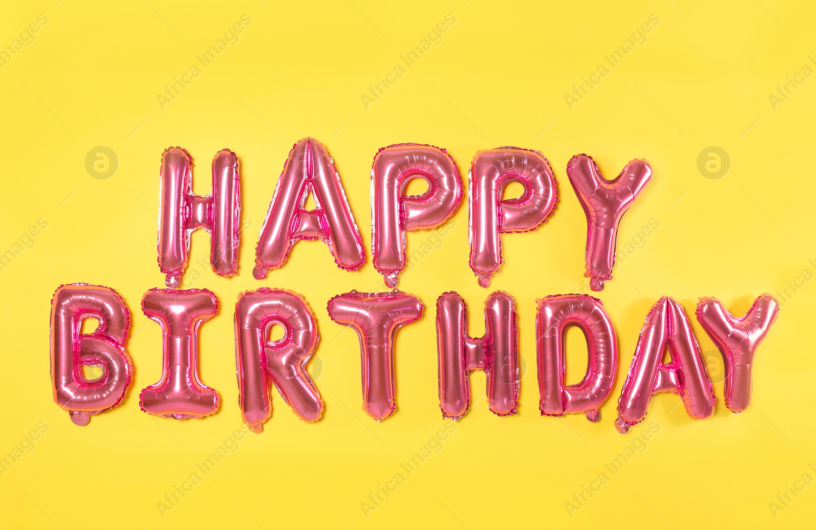 Photo of Phrase HAPPY BIRTHDAY made of pink foil balloon letters on yellow background