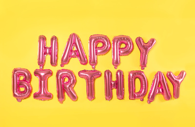 Phrase HAPPY BIRTHDAY made of pink foil balloon letters on yellow background