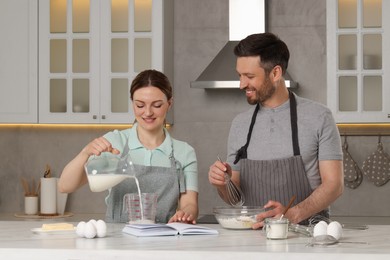 Happy couple cooking by recipe book in kitchen