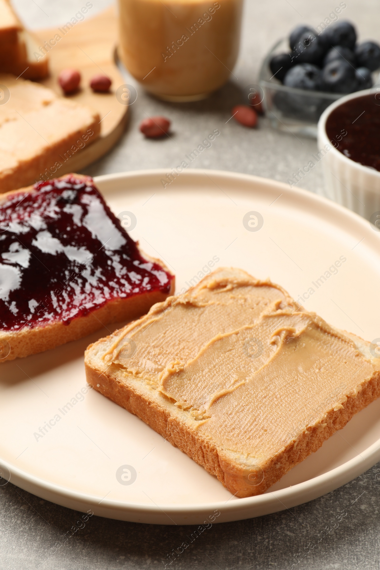 Photo of Tasty peanut butter sandwiches with jam on gray table, closeup