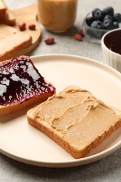 Photo of Tasty peanut butter sandwiches with jam on gray table, closeup