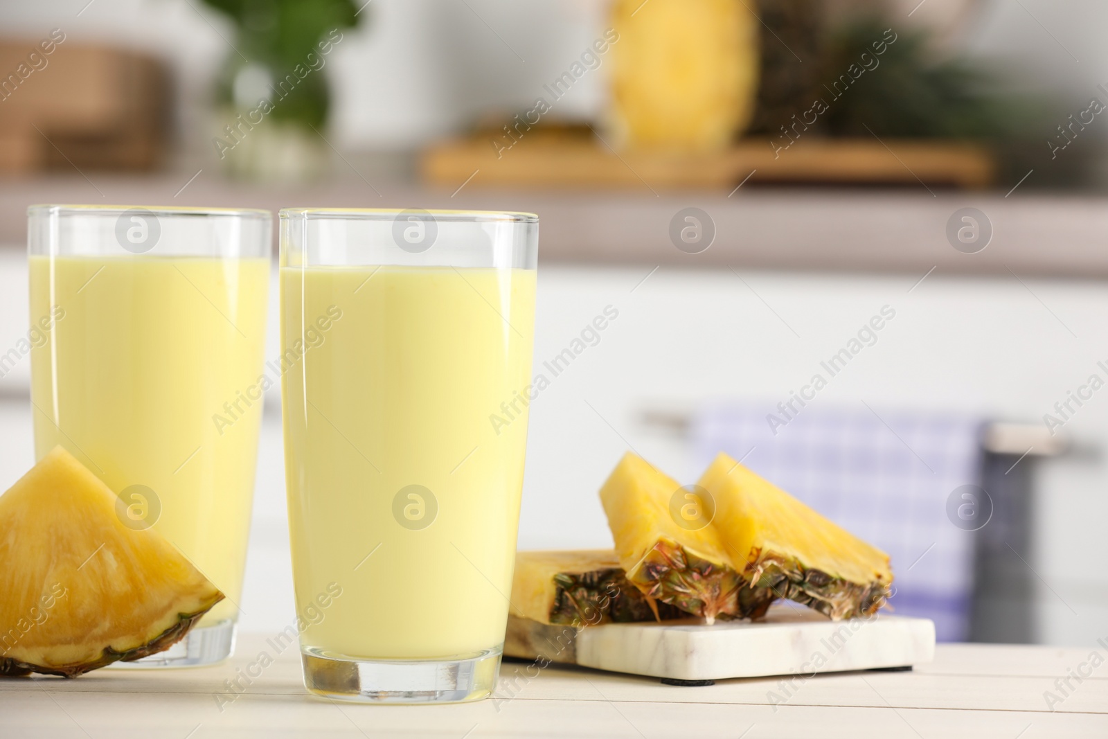 Glasses of tasty pineapple smoothie and cut fruit on white table indoors, space for text Photo of Glasses of tasty pineapple smoothie and cut fruit on white table indoors, space for text