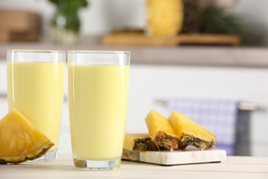 Photo of Glasses of tasty pineapple smoothie and cut fruit on white table indoors, space for text