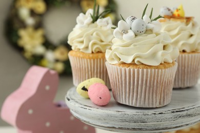 Tasty Easter cupcakes with vanilla cream and candies on cake stand, closeup