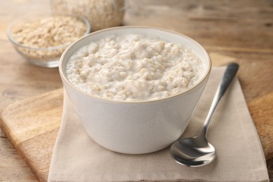 Photo of Tasty boiled oatmeal in bowl and spoon on wooden table, closeup