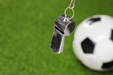 Football referee equipment. Metal whistle and soccer ball on green grass, closeup with space for text