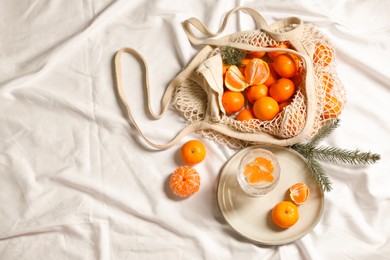 Photo of Delicious ripe tangerines, glass with sparkling wine and fir branch on white bedsheet, flat lay. Space for text