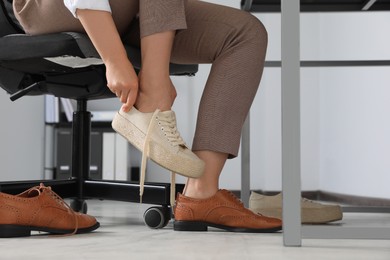 Woman taking off uncomfortable shoes and putting on sneakers in office, closeup