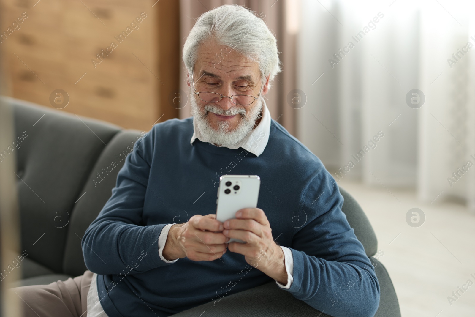 Photo of Portrait of happy grandpa with glasses using smartphone indoors