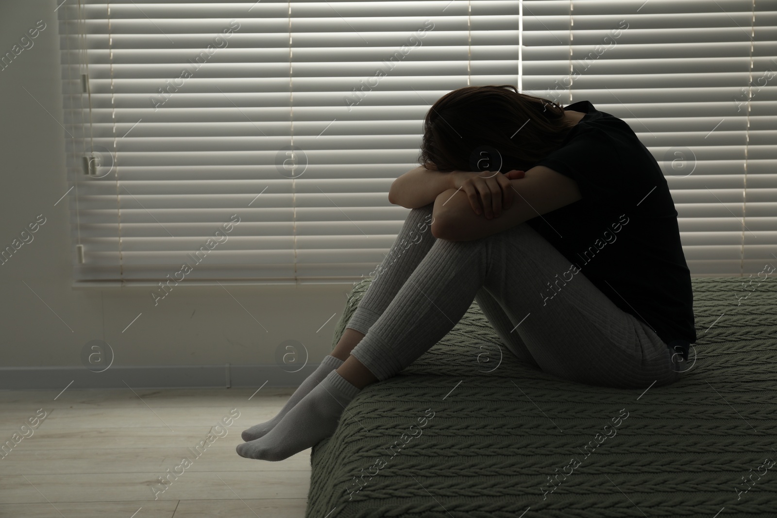 Photo of Sad young woman sitting on bed at home, space for text