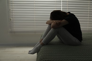 Sad young woman sitting on bed at home, space for text