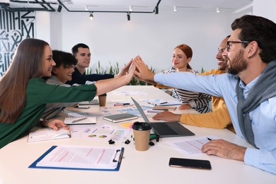 Photo of Team of employees joining hands at white table in office. Startup project
