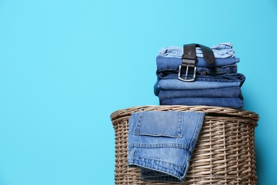 Stack of different jeans on basket against color wall with space for text