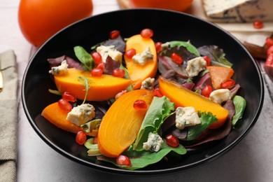 Photo of Delicious persimmon salad with pomegranate and spinach on table, closeup